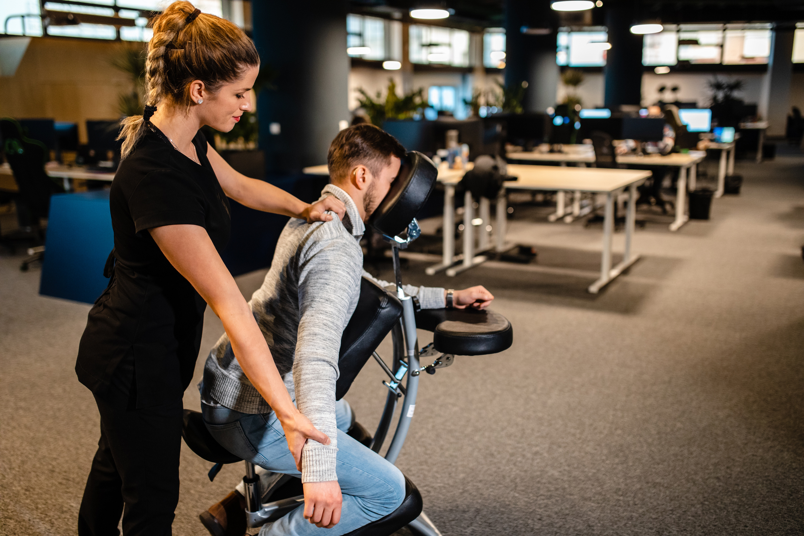 Personal corporate masseuse giving a back massage to a tired web designer on a mobile massage chair